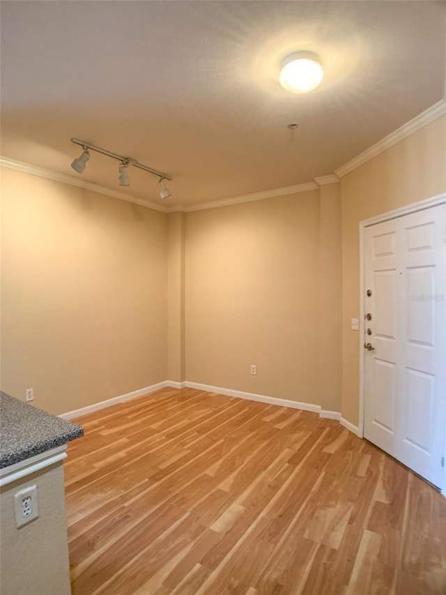 spare room with track lighting, ornamental molding, baseboards, and light wood-type flooring