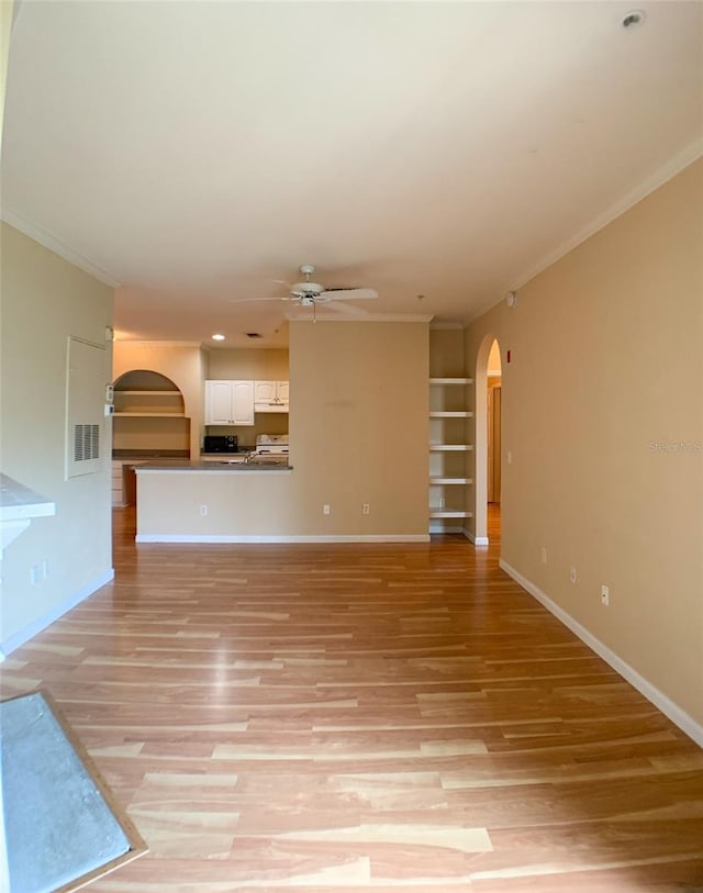 unfurnished living room with crown molding, arched walkways, and a ceiling fan