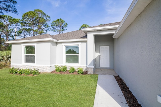 doorway to property with a lawn, roof with shingles, stone siding, and stucco siding