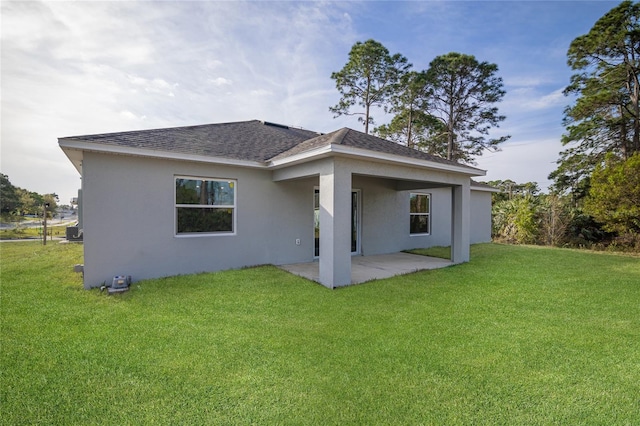 rear view of house featuring roof with shingles, a patio, stucco siding, and a yard