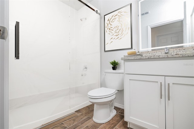 bathroom with wood finish floors, vanity, toilet, visible vents, and a stall shower