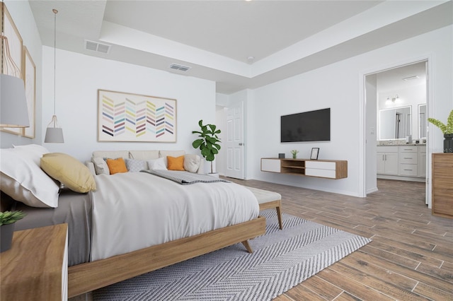 bedroom with visible vents, a raised ceiling, ensuite bathroom, and wood finished floors
