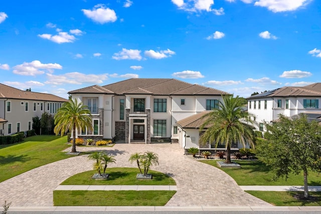 back of house with curved driveway, a lawn, stucco siding, and a balcony