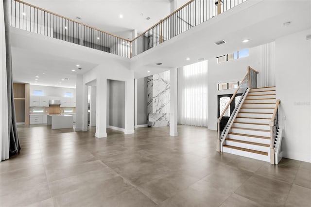 unfurnished living room featuring baseboards, stairway, visible vents, and a towering ceiling