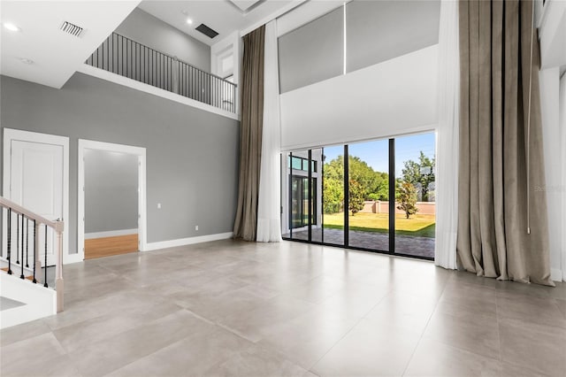 unfurnished living room with a towering ceiling, stairs, baseboards, and visible vents