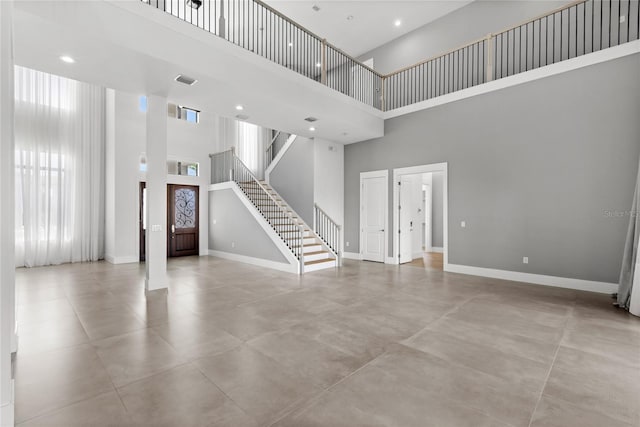 unfurnished living room with baseboards, stairs, finished concrete flooring, and a high ceiling