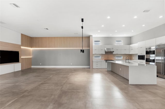 kitchen with modern cabinets, a sink, wall chimney range hood, stainless steel appliances, and a large island with sink