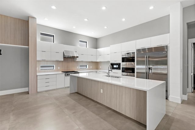 kitchen with built in appliances, light countertops, wall chimney range hood, and modern cabinets