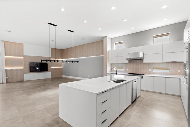 kitchen featuring a sink, wall chimney range hood, a kitchen island with sink, backsplash, and modern cabinets