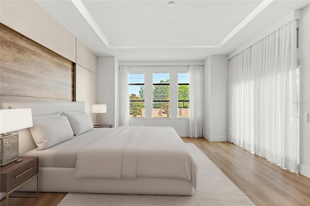 bedroom with light wood finished floors and a tray ceiling