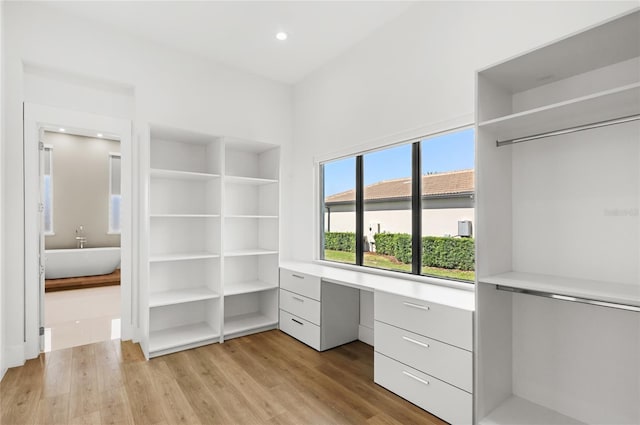 walk in closet featuring light wood finished floors and built in desk