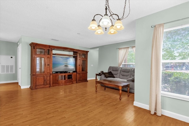 living room featuring baseboards, a textured ceiling, light wood-style flooring, and a chandelier