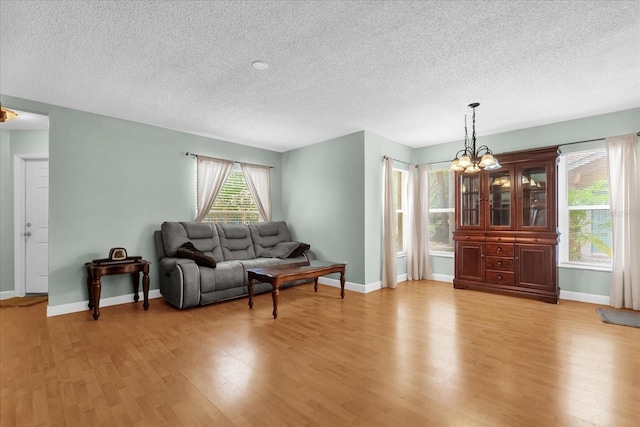 living area with an inviting chandelier, baseboards, light wood finished floors, and a textured ceiling