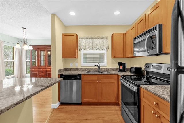 kitchen with light wood-style floors, a chandelier, a sink, stone counters, and stainless steel appliances