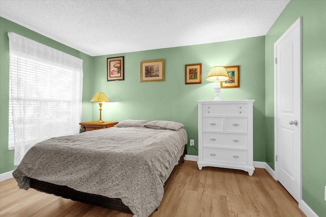 bedroom featuring baseboards, a textured ceiling, and light wood finished floors