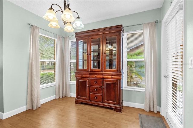 entryway featuring baseboards, a wealth of natural light, light wood-style flooring, and a chandelier