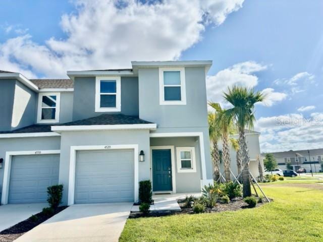 view of property with a garage, stucco siding, concrete driveway, and a front lawn