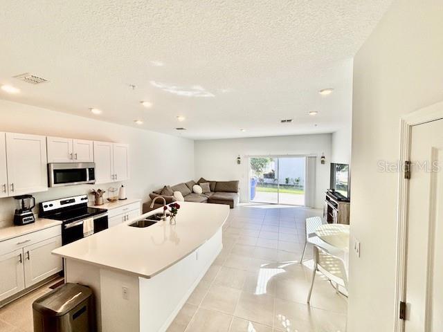 kitchen with a center island with sink, a sink, white cabinets, open floor plan, and stainless steel appliances