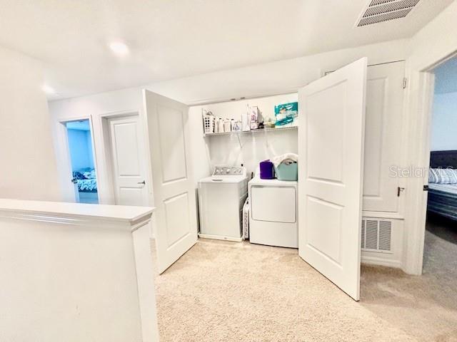 laundry room featuring visible vents, light carpet, and washer and dryer