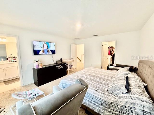 carpeted bedroom with visible vents, connected bathroom, a spacious closet, and a closet