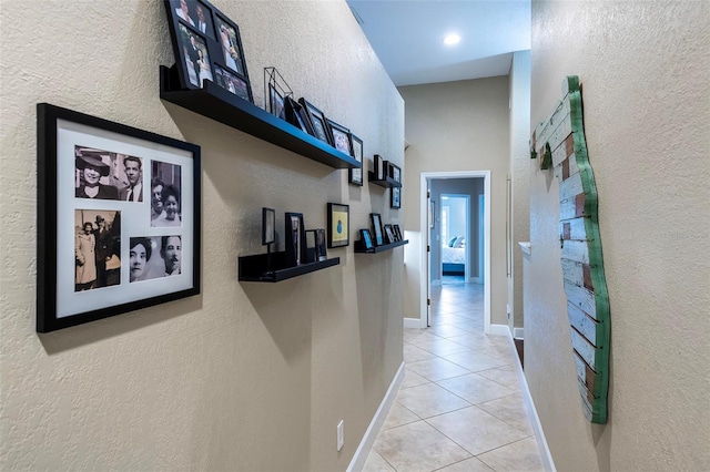 hallway featuring light tile patterned floors, baseboards, and a textured wall