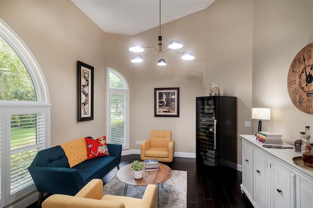 living room featuring beverage cooler, baseboards, dark wood-style flooring, a chandelier, and high vaulted ceiling