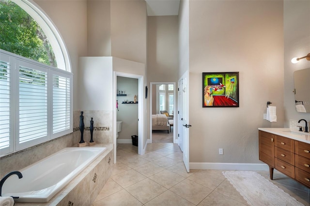 ensuite bathroom with baseboards, a bath, vanity, and a towering ceiling
