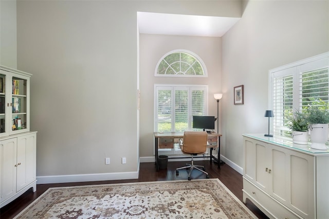 office area featuring a towering ceiling, baseboards, and dark wood-style floors