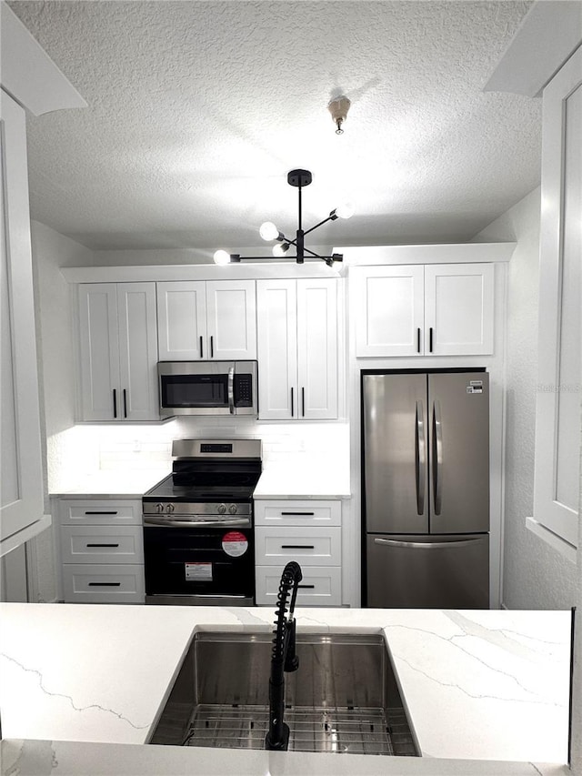 7147 Yacht Basin Ave Unit 119, Orlando, FL 32835 - kitchen featuring a sink, an inviting chandelier, a textured ceiling, and appliances with stainless steel finishes