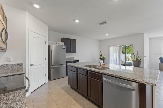 kitchen featuring light stone countertops, a sink, stainless steel appliances, visible vents, and a center island with sink