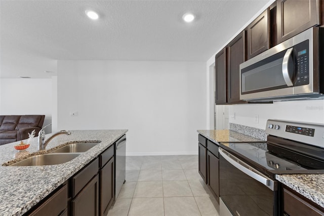 kitchen featuring dark brown cabinets, light stone countertops, a sink, stainless steel appliances, and baseboards