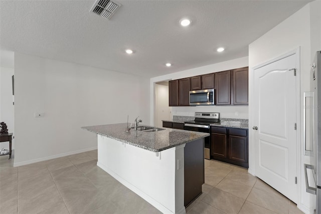 kitchen featuring a breakfast bar, a kitchen island with sink, dark stone countertops, stainless steel appliances, and visible vents