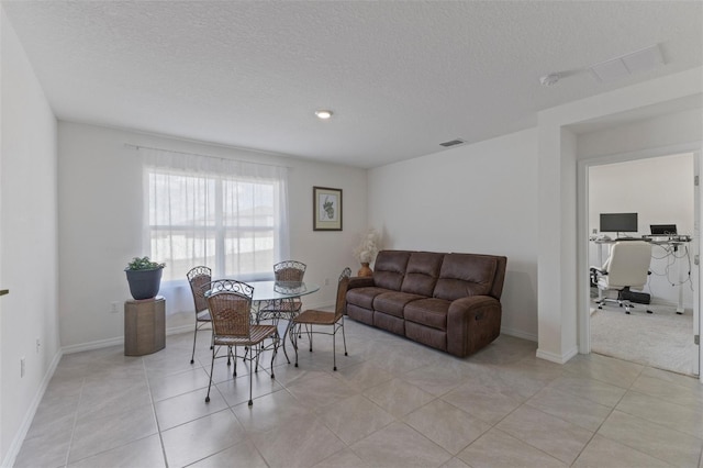 living area with light tile patterned flooring, a textured ceiling, visible vents, and baseboards