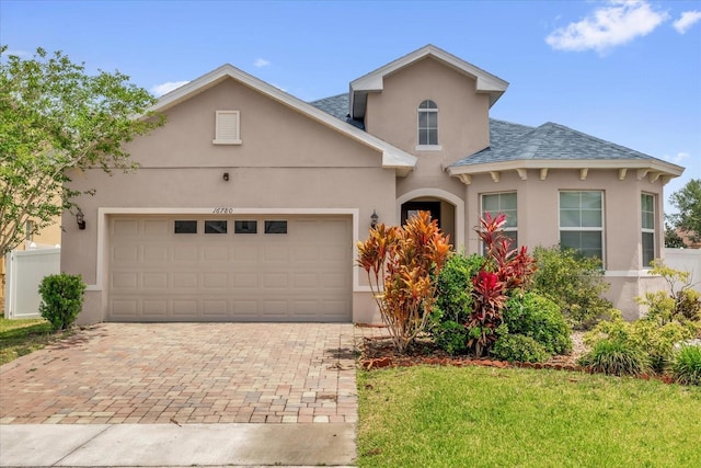 16780 Meadows St, Clermont, FL 34714 - view of front facade with stucco siding, decorative driveway, an attached garage, a shingled roof, and a front lawn