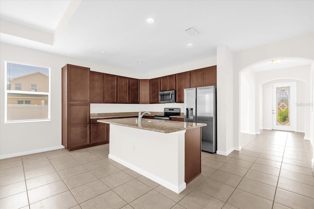 16780 Meadows St, Clermont, FL 34714 - kitchen with appliances with stainless steel finishes, arched walkways, light tile patterned flooring, a center island with sink, and light stone countertops