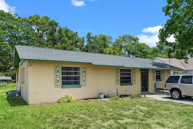 single story home with roof with shingles, concrete block siding, and a front yard