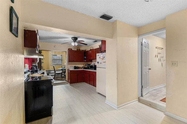 kitchen with freestanding refrigerator, range hood, visible vents, and a textured ceiling