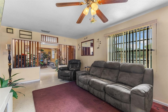 living area with a textured ceiling, visible vents, baseboards, and ceiling fan