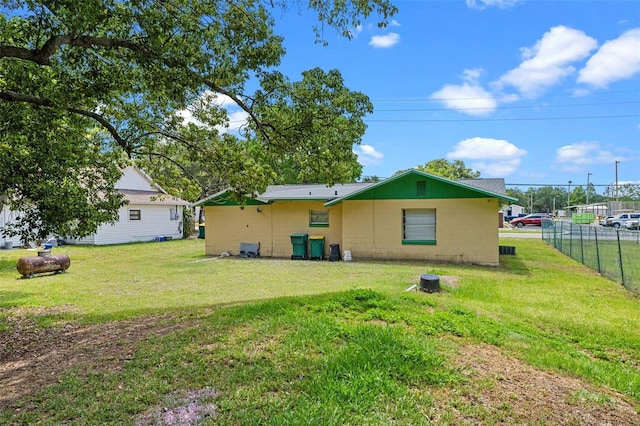 rear view of house with fence, concrete block siding, and a lawn
