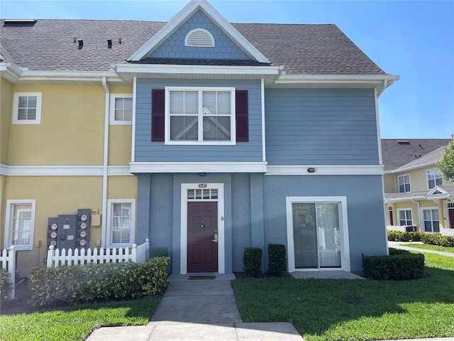multi unit property with roof with shingles, stucco siding, and a front lawn