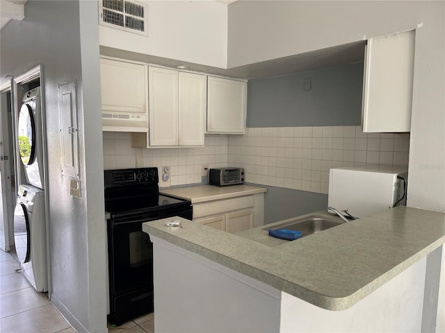 kitchen featuring stacked washer / drying machine, black electric range oven, light tile patterned floors, under cabinet range hood, and visible vents