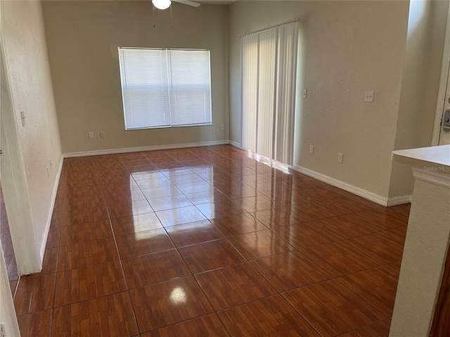 empty room featuring baseboards, ceiling fan, and dark tile patterned floors