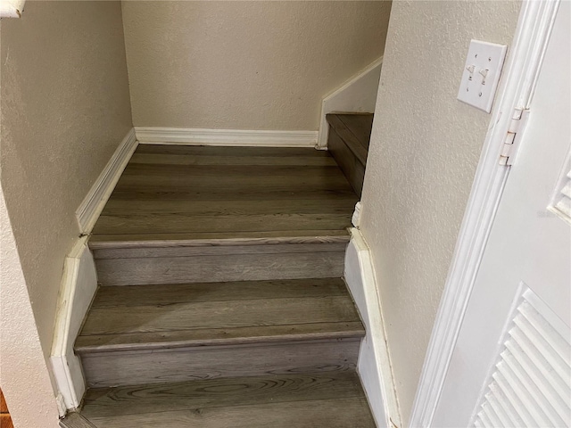 staircase featuring baseboards, a textured wall, and wood finished floors