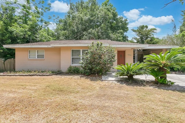 ranch-style home with concrete block siding, fence, a front yard, and a carport
