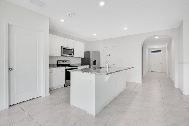 kitchen with visible vents, arched walkways, a center island with sink, a sink, and stainless steel appliances