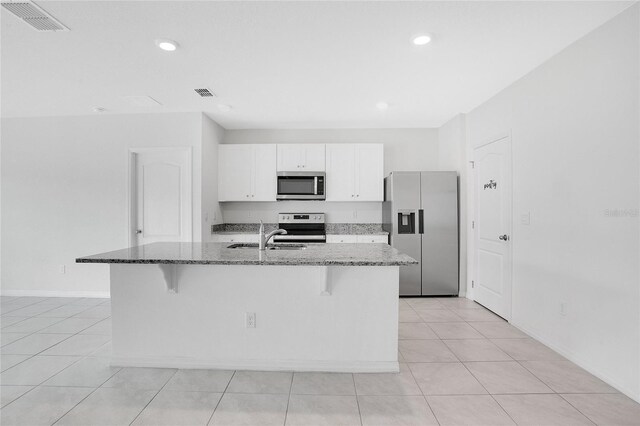 kitchen with a kitchen bar, visible vents, white cabinets, dark stone counters, and stainless steel appliances
