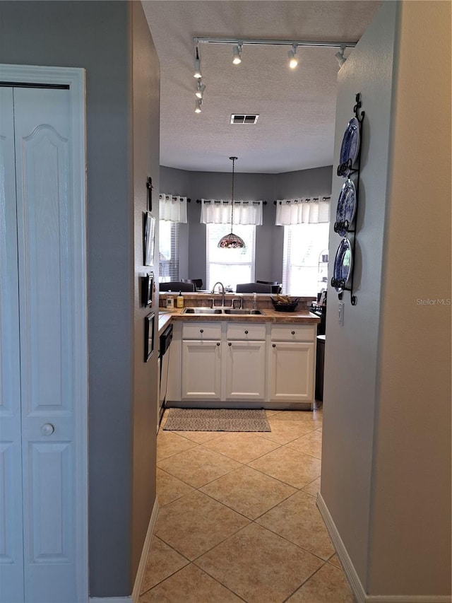 kitchen featuring visible vents, rail lighting, a sink, white cabinets, and light tile patterned flooring