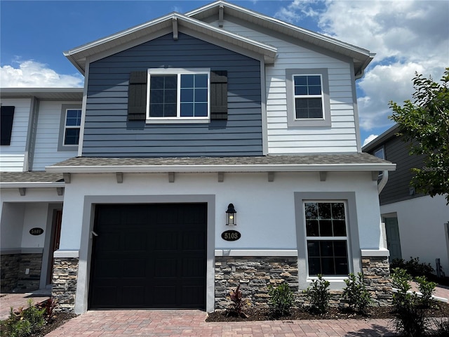view of front of house with an attached garage, stone siding, roof with shingles, and decorative driveway