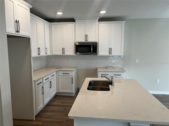 kitchen with stainless steel microwave, a sink, a center island with sink, dark wood-style floors, and white cabinets