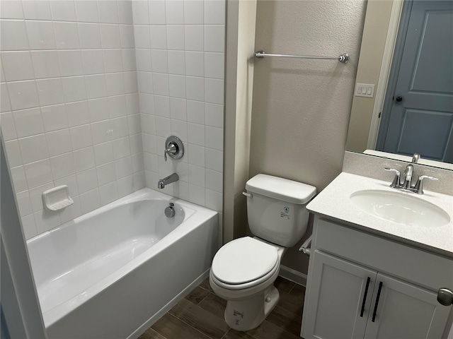 bathroom featuring toilet, vanity, tub / shower combination, wood finish floors, and a textured wall